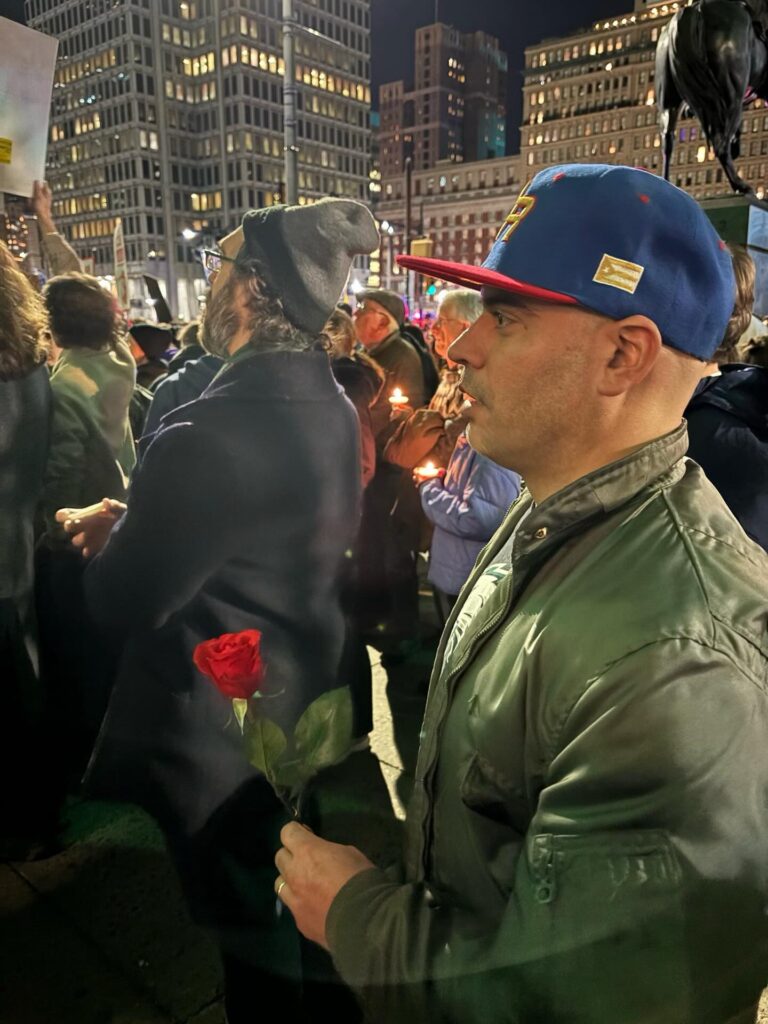 Pablo Iván McConnie-Saad, con una rosa roja en mano y un gorro que rinde homenaje a su herencia puertorriqueña, participa en una vigilia nocturna, mostrando su compromiso y solidaridad con la comunidad.